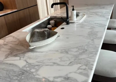 A kitchen with white marble counter tops and stools.
